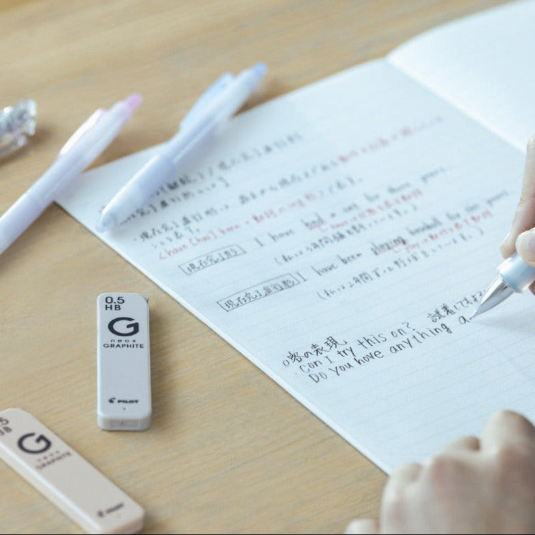 Person writing on a piece of paper with a pen, surrounded by stationery items on a wooden surface.