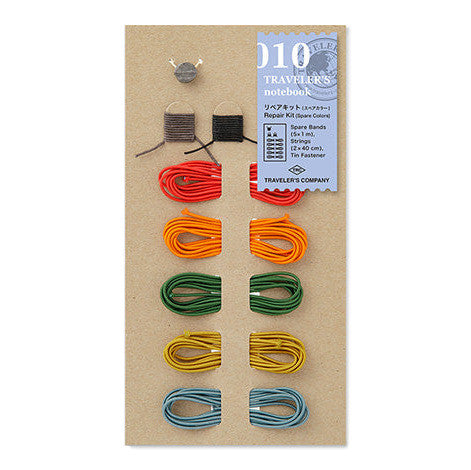 Traveler's Company Notebook repair kit with colorful elastics, bookmark strings, and clasp on a kraft card