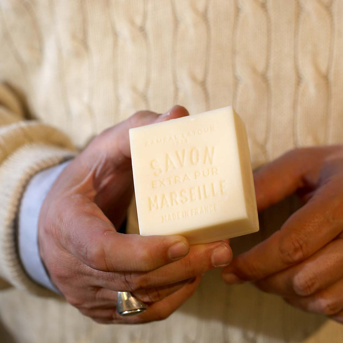 Close-up of man holding the 150g bar of soap to show the relative size. He wears a cream knitted jumper